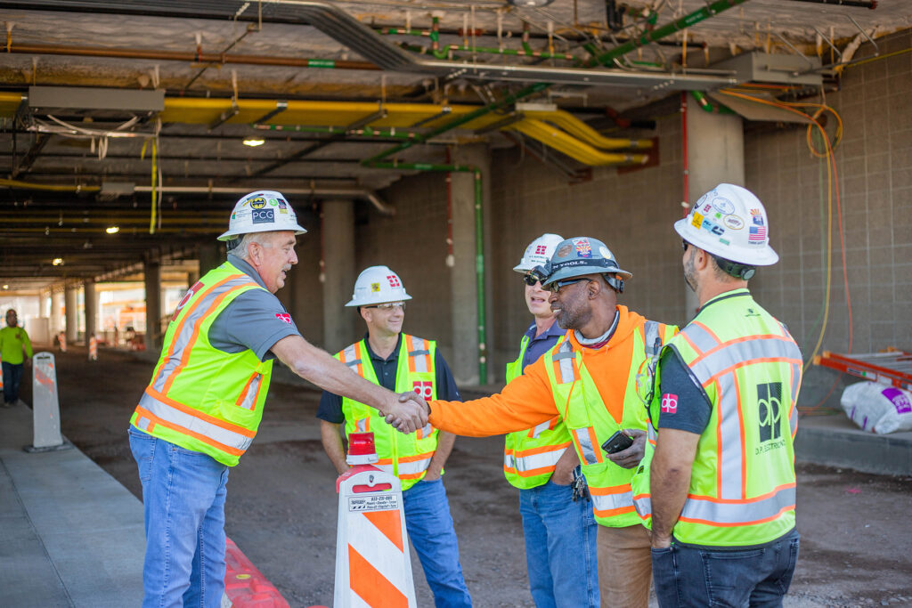 A group of construction workers shaking hands in front of a building.