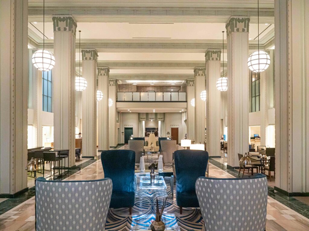 The lobby of a hotel with blue chairs and a chandelier projects elegance.