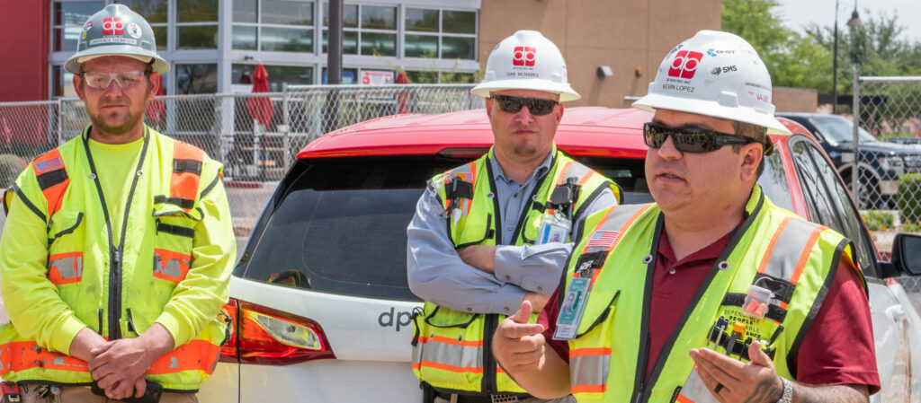 Three construction workers standing in front of a new car.