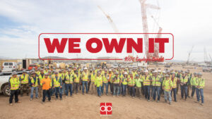 A group of construction workers posing for a photo, proudly displaying their career path in the construction industry with the words "We own it.